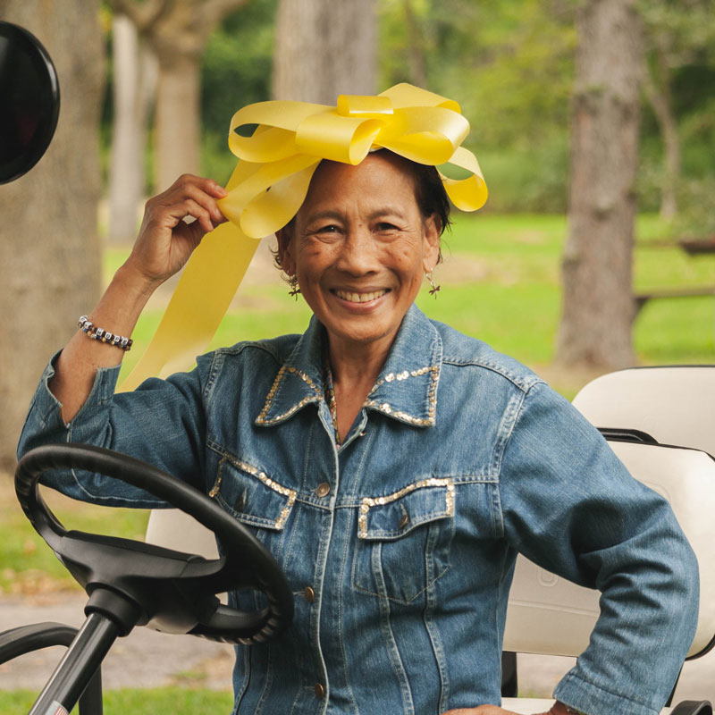Individual placing a big yellow bow on her head while sitting on a golf cart