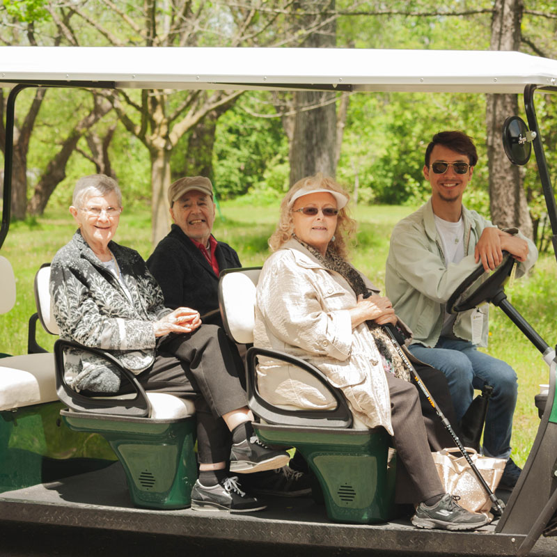 Group of older adults and sunshine staff enjoying the day on a golf cart