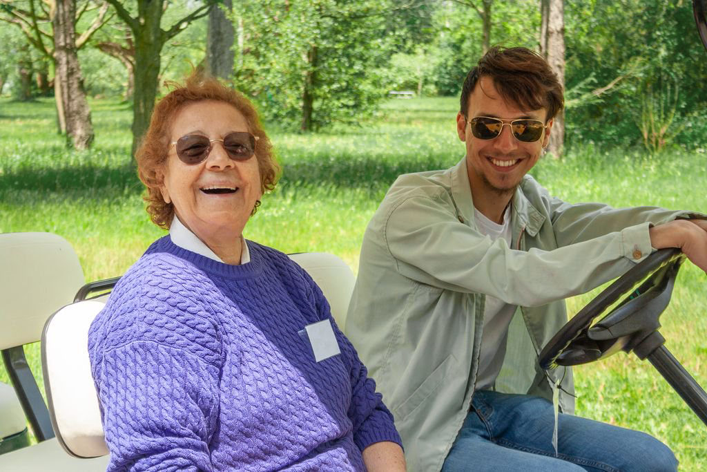 A Sunshine Centres' staff member and a participant sit on a golf cart on a sunny day.